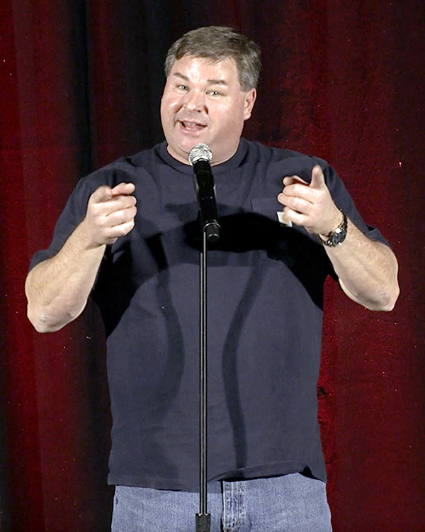 A man speaking in front of a microphone stand that is looking directly into the camera.